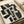 Abstract geometric artwork featuring bold black and beige intersecting rectangular shapes creating a maze-like pattern. The painting uses thick brushstrokes with visible texture on canvas, showing architectural forms and negative space. Artist signature visible in bottom right corner. The artwork is displayed on a light wooden frame against neutral wrapping paper and ribbon, showing the piece ready for gifting.