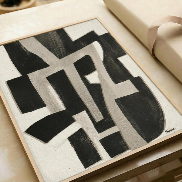 Abstract geometric artwork featuring bold black and beige intersecting rectangular shapes creating a maze-like pattern. The painting uses thick brushstrokes with visible texture on canvas, showing architectural forms and negative space. Artist signature visible in bottom right corner. The artwork is displayed on a light wooden frame against neutral wrapping paper and ribbon, showing the piece ready for gifting.