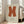 May include: Large framed poster with orange X shape on cream background, displayed in bright living room with beige sofa, white walls, and tall windows. Poster shows exhibition text for Ellsworth Kelly at Ferus Gallery Los Angeles. Light wooden frame sits on hardwood floor against window, creating warm natural lighting and shadows.