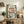 May include: Framed poster with three red fish swimming among green foliage and coral pink flowers on cream background, displayed on rustic wooden sideboard beside fern plant, books, and ceramic vases in cozy living room setting with beige armchair and floating shelf