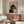 May include: Framed poster on wall above wooden credenza featuring black and tan dachshund wearing pearl necklace on pink background with "DOGUE" text in orange letters, styled like fashion magazine cover. Modern living room setting with white upholstered chair, round glass coffee table, and floor lamp.