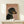 May include: Framed poster featuring a black and tan dachshund wearing a rhinestone collar on dusty pink background with "DOGUE" text in orange letters, displayed on light wood surface next to small white wrapped gift with twine bow against cream wall