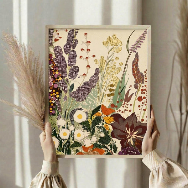 May include: Person in cream ruffled sleeves holding framed botanical art print and dried pampas grass against white curtained window. The artwork features dotted wildflowers, daisies, and plants in purple, yellow, green, and orange colors with pointillism-style dots throughout. Natural lighting creates soft shadows on the cream-colored wall.
