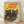 May include: Framed vintage-style poster featuring three black cats with bright yellow-green eyes against a sunset sky. Red "JAPAN WEEK" text spans the top, with orange cherry blossom branches in foreground and flying bird silhouette. Poster has weathered, retro aesthetic with warm yellow, orange and teal colors. Light wood frame sits on wooden floor against white wall with soft shadows.