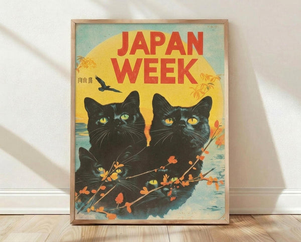 May include: Framed vintage-style poster featuring three black cats with bright yellow-green eyes against a sunset sky. Red "JAPAN WEEK" text spans the top, with orange cherry blossom branches in foreground and flying bird silhouette. Poster has weathered, retro aesthetic with warm yellow, orange and teal colors. Light wood frame sits on wooden floor against white wall with soft shadows.