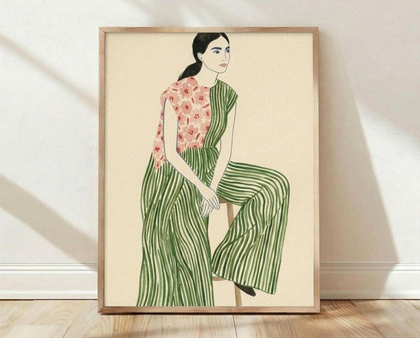 May include: Framed poster print leaning against white wall on wooden floor. Artwork shows woman with black ponytail sitting in green and white striped wide-leg pants and pink floral top. Illustration has vintage-inspired flat color style on cream background. Natural wood frame surrounds the print. Soft shadows cast on textured white wall behind.