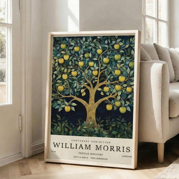 May include: Framed poster featuring William Morris-style apple tree design with golden fruit and green foliage on dark background, exhibition text at bottom reading "Centenary Exhibition William Morris 1934 Textile Industry London Jan 6 to May 6 Free Admission." Light wood frame leaning against white wall next to beige upholstered sofa in bright room with large windows.