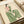 May include: Illustration of a seated woman in striped green pants and floral pink top, rendered in minimalist style with clean lines on cream background. The artwork is displayed in a light wood frame, positioned against wrapped packages with neutral ribbon on a white surface.