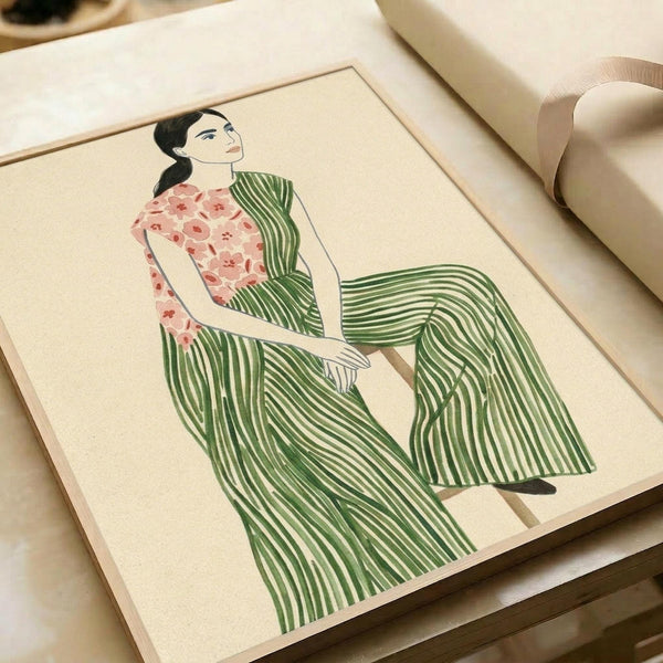 May include: Illustration of a seated woman in striped green pants and floral pink top, rendered in minimalist style with clean lines on cream background. The artwork is displayed in a light wood frame, positioned against wrapped packages with neutral ribbon on a white surface.