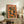 May include: Orange vintage-style travel poster featuring woman with dark hair surrounded by citrus fruits and green leaves, displayed in light wooden frame on rustic wooden sideboard next to fern plant, books, and ceramic vessels in bright living room setting