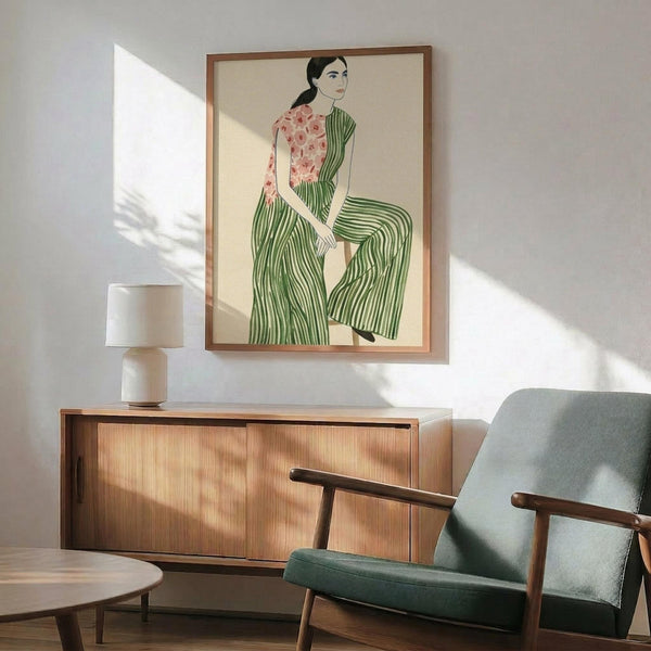 May include: Framed poster print featuring woman in green striped pants and pink floral top, displayed above wooden sideboard with ceramic table lamp in modern living room setting with mid-century green upholstered chair and round coffee table, natural sunlight creating shadows on white wall