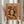 May include: Framed orange and green art print held by person in cream clothing, featuring stylized woman with closed eyes surrounded by citrus fruits and leaves, displayed near dried pampas grass against white curtained window