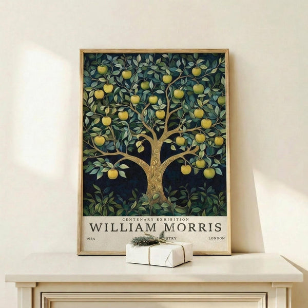 May include: Framed poster of an ornate apple tree with golden fruit and green foliage against a dark blue background, displayed on a light wooden shelf next to a small wrapped gift with twine and evergreen sprig. The vintage-style botanical artwork features decorative text reading "CENTENARY EXHIBITION WILLIAM MORRIS 1934 LONDON" at the bottom in a cream-colored border.