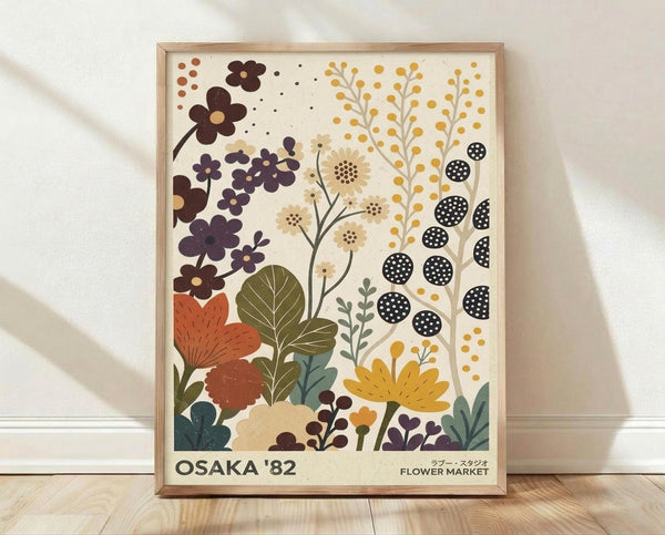 May include: Framed botanical poster with stylized flowers and plants in earthy tones of rust orange, golden yellow, deep purple, and olive green against cream background. Features geometric and organic floral motifs with "OSAKA '82" and "FLOWER MARKET" text at bottom. Natural wood frame sits on light wooden floor against white wall with soft natural lighting.