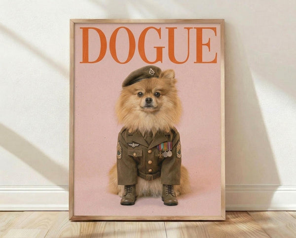 May include: Framed poster print featuring a fluffy orange Pomeranian dog dressed as a military officer in olive green uniform with medals, beret, and boots against pink background. The word "DOGUE" appears in large orange letters at top. Light wood frame rests on wooden floor against white wall with natural lighting casting shadows.