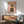 May include: Framed poster print featuring a fluffy Pomeranian dog dressed in olive green military uniform with cap, medals and boots against pink background, displayed on white wall above wooden sideboard with ceramic lamp, next to sage green mid-century modern armchair in naturally lit room