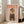 May include: Framed poster with pink background showing fluffy Pomeranian dog wearing olive green military uniform with medals, beret, and combat boots. Orange "DOGUE" text at top mimics fashion magazine style. Light wooden frame leans against white wall next to beige sofa in bright, minimalist living room with hardwood floors and large windows.