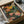 May include: Framed botanical art print featuring stylized mushrooms and foliage in coral, orange, pink, and green tones on dark background. Print displayed in black frame, nestled in cardboard shipping box with brown paper padding. Warm earth tone palette with dotted patterns and organic shapes creates mid-century modern aesthetic.