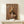 May include: Framed poster displaying a spaniel dog's head digitally placed on a human body wearing a tan blazer with small flower lapel pin, styled as fashion magazine cover with "DOGUE" text at top in beige letters on brown background. Small white wrapped gift with greenery sits on light wood console table below the natural wood framed artwork against cream wall.