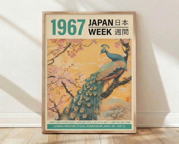 May include: Framed vintage-style poster featuring a vibrant peacock perched on cherry blossom branches against a golden sunset sky. The artwork shows traditional Japanese ukiyo-e style with Mount Fuji in the background. Text reads "1967 JAPAN WEEK" in teal and black lettering. The poster is displayed in a light wood frame, leaning against a white wall on light wooden flooring with soft natural lighting creating gentle shadows.