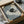 May include: Framed print showing black cat curled up on blue and white striped bedding holding a white coffee cup, displayed in black frame being unpacked from cardboard shipping box with protective wrapping on white surface.