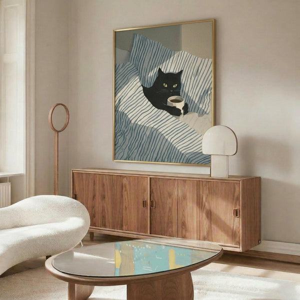 May include: Framed poster of black cat with yellow eyes holding coffee cup on blue and white striped bedding, displayed above wooden credenza in modern living room with white curved chair, glass coffee table, and table lamp