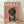 May include: Framed poster print leaning against white wall on wooden floor. Features black and tan dachshund wearing pink chef's hat and heart-patterned apron on dusty rose background. Large white "DOGUE" text at top mimics fashion magazine style. Natural wood frame with soft shadows cast on cream colored wall behind.