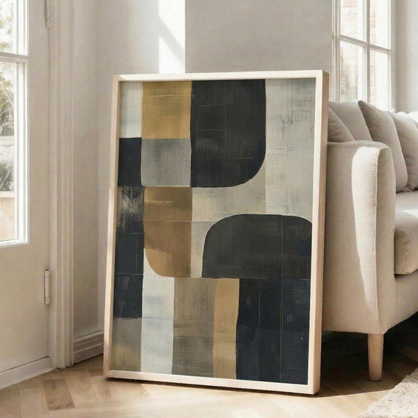 May include: Framed abstract geometric artwork with dark green, mustard yellow, cream and gray color blocks in modern living room setting. Art piece leans against beige sofa near tall windows with natural light streaming across wooden floors.