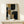 May include: Abstract geometric artwork in natural wood frame displaying overlapping curved and rectangular shapes in navy blue, mustard yellow, gray, and cream tones with textured brushwork effects, displayed on light wood console table beside small white wrapped gift with natural greenery accent against cream wall