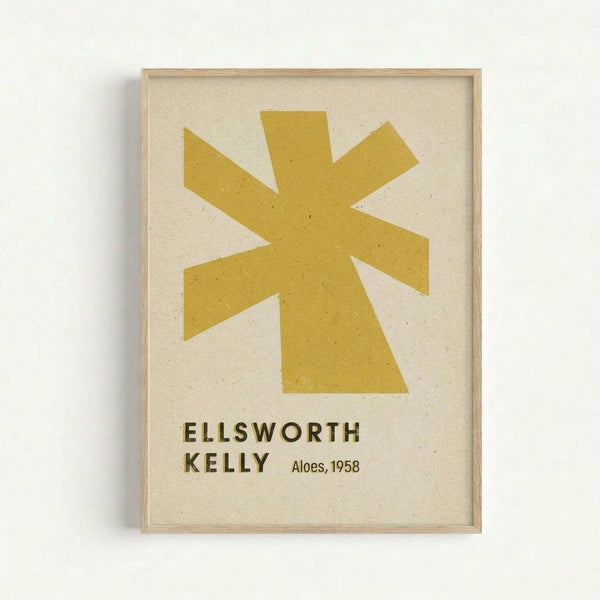 Framed art print featuring a golden yellow star-like shape with eight pointed rays on cream speckled paper background. Text below reads "ELLSWORTH KELLY" and "Aloes, 1958" in dark letters. The minimalist geometric design is displayed in a light wood frame against a white wall.