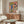 May include: Colorful still life poster with coral pink background featuring sunflowers in blue vase, wine bottle and glass, fish platter with olives and fruit, and pasta bowl, displayed above mid-century walnut credenza in modern living room with cream chair, glass coffee table, and white mushroom lamp