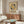 May include: Framed Bauhaus exhibition poster with geometric design featuring yellow and black circles around striped cross pattern on cream background, displayed above walnut sideboard in modern living room with white curved chair, brass floor lamp, oval glass coffee table, and white mushroom table lamp.