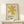 May include: Framed art print featuring a golden yellow abstract star or asterisk shape on cream background, displayed on light wood console table against white wall. Small wrapped gift box with evergreen sprig sits beside the natural wood frame. Minimalist Scandinavian-style interior setting with clean lines and neutral tones.