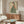 May include: Japanese woman artwork in wooden frame above mid-century walnut credenza. Woman wears green striped kimono with coral floral sleeves, holding persimmon fruit. Cream textured background. Modern living room setting with white curved chair, glass coffee table, floor lamp. Soft natural lighting creates warm shadows on furniture.