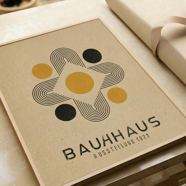 Modernist poster design featuring abstract geometric composition with intersecting curved linear elements forming a symmetrical pattern around yellow and dark green circles on beige textured paper background, displaying "BAUHAUS AUSSTELLUNG 1923" text below the artwork, shown lying flat on white surface with rolled paper visible at edges