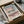 May include: Framed Bauhaus architecture poster with geometric pink and teal building design, displayed in wooden frame inside cardboard shipping box with protective wrapping paper and wooden support pieces