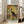 May include: Framed vintage-style poster leaning against white wall next to beige sofa in sunlit room. Print features silhouette of long-necked wading bird against warm yellow sun with painterly brushstrokes in orange, green, and brown tones. Text reads "Wetland Ecology Field Guide" and "Mid-Century Marshland Vintage Print Series" in dark lettering on textured background resembling canvas or linen.