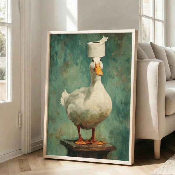 May include: Framed artwork featuring a white duck with orange bill and feet standing on wooden platform, balancing toilet paper roll on its head, painted in realistic style against textured teal-green background, displayed in light wood frame leaning against white wall next to beige upholstered chair in bright living room setting.