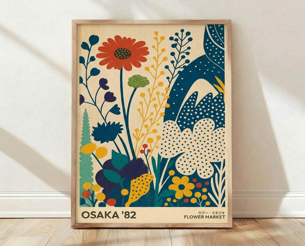 May include: Framed art print leaning against white wall on light wood floor. Poster features stylized botanical illustration with vibrant flowers and plants in retro folk art style. Design shows orange daisy, blue polka-dotted leaves, yellow wildflowers, green foliage, and purple blooms on cream background. Text reads "OSAKA '82" and "FLOWER MARKET" at bottom. Natural wood frame with thin border. Soft shadows cast on textured white wall.