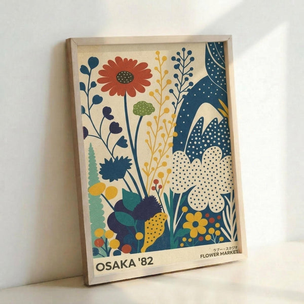 May include: Framed vintage-style poster with botanical illustration featuring colorful stylized flowers and plants in blues, oranges, greens, and yellows on cream background. Design shows various blooms, leaves, and stems with polka dot patterns throughout. Text reads "OSAKA '82 FLOWER MARKET" at bottom. Light wood frame displayed against white wall on light surface.