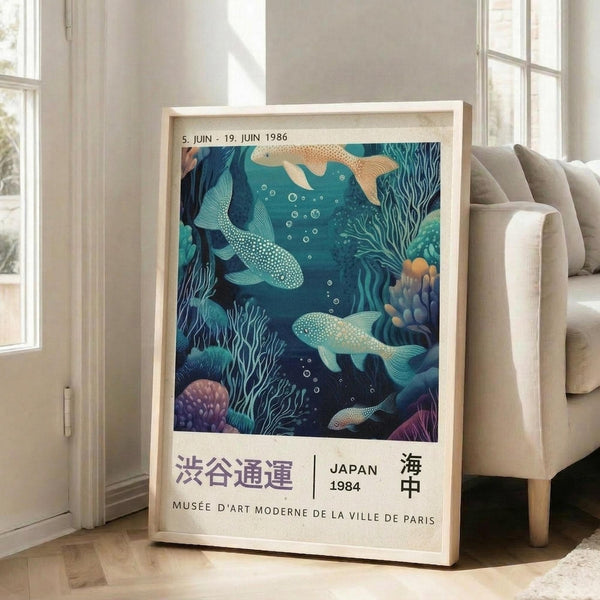 May include: Framed vintage-style exhibition poster featuring underwater scene with whales, coral, and sea life in deep blues, teals, and purple tones. Japanese and French text at bottom with dates from 1986. Light wood frame leaning against white wall next to beige sofa in bright, modern living room with large windows.