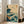 May include: Framed poster with Japanese-inspired ocean waves in teal and cream colors, featuring dramatic crashing waves, rocky coastline, flying birds, and red text seal, displayed against white wall next to beige upholstered chair in bright living room with windows.