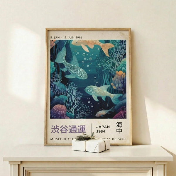 May include: Framed vintage-style exhibition poster featuring underwater scene with spotted whales, coral, and seaweed in blue and teal tones, displayed on light wood shelf next to small wrapped gift with pine sprig, against cream wall with soft natural lighting