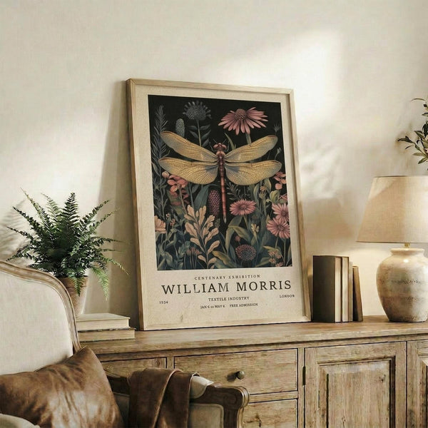 May include: A framed botanical poster featuring a large golden dragonfly surrounded by pink flowers and green foliage on a dark background, displayed on a rustic wooden sideboard next to books, a ceramic vase, and a potted fern in a cozy living room setting with neutral walls and brown leather furniture.