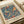 Vintage exhibition poster featuring William Morris's Strawberry Thief pattern with two colorful birds perched among strawberry vines, flowers, and foliage on a deep blue background. The decorative textile design is framed by cream borders with exhibition text above and below. The poster lies flat on white paper with a cream ribbon visible, showing the Arts and Crafts movement's characteristic botanical motifs in rich reds, oranges, and greens.