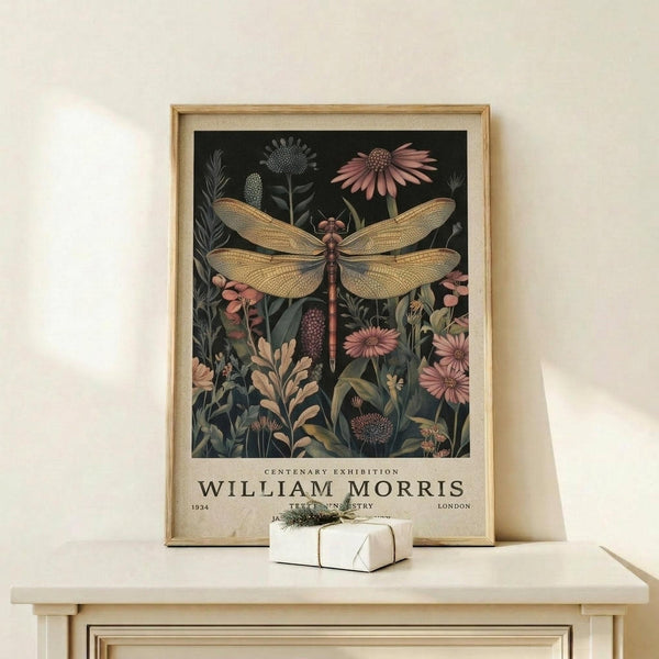 May include: Framed botanical poster featuring large golden dragonfly with detailed wings surrounded by wildflowers and plants in muted pink, green, and cream tones against dark background. Light wood frame displays vintage exhibition text below artwork. Small wrapped gift box sits on natural wood shelf beneath frame against cream wall with soft natural lighting.