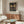 May include: Framed vintage-style botanical poster featuring golden dragonfly with detailed wings surrounded by pink flowers and green foliage on dark background, displayed above mid-century modern walnut credenza with brass handles in minimalist living room with cream walls, white upholstered chair, and oval glass coffee table