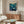 May include: Framed vintage Japanese exhibition poster featuring underwater scene with whales, coral, and sea life in blues and teals, displayed above walnut credenza in modern living room with white sculptural chair, marble table lamp, glass coffee table, and cream textured rug on light wooden floors.