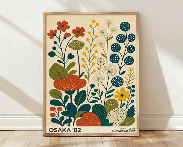 May include: Framed botanical poster print with stylized flowers and plants in retro mid-century modern style, featuring orange, yellow, teal, and olive green colors on cream background. Wooden frame leans against white wall on light wood floor with soft natural lighting and shadows.