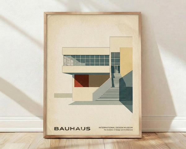 May include: Framed poster print featuring modernist architectural illustration in muted tones of cream, teal, yellow and rust red. Shows geometric building with grid windows, curved staircase, and angular forms in Bauhaus style. Natural wood frame sits on light wooden floor against white textured wall with soft shadows.